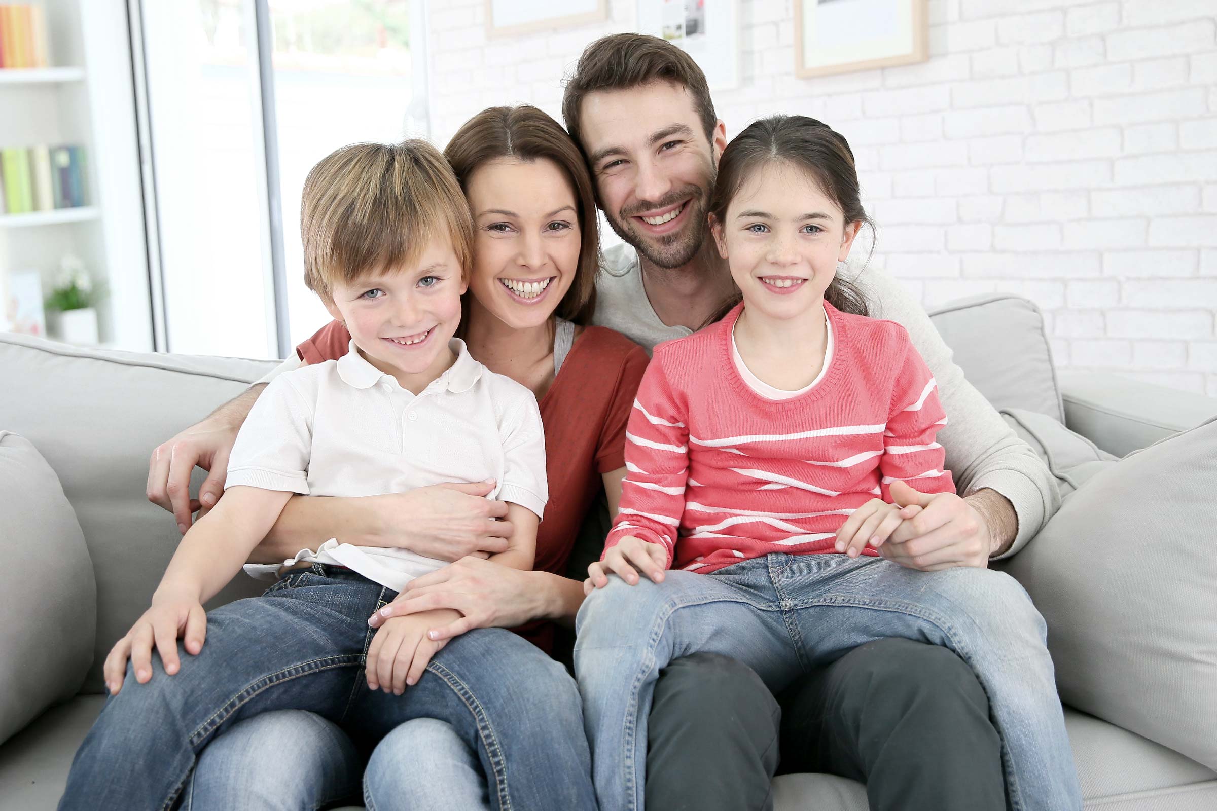 junge familie mit zwei kindern sitzen lachend auf dem sofa