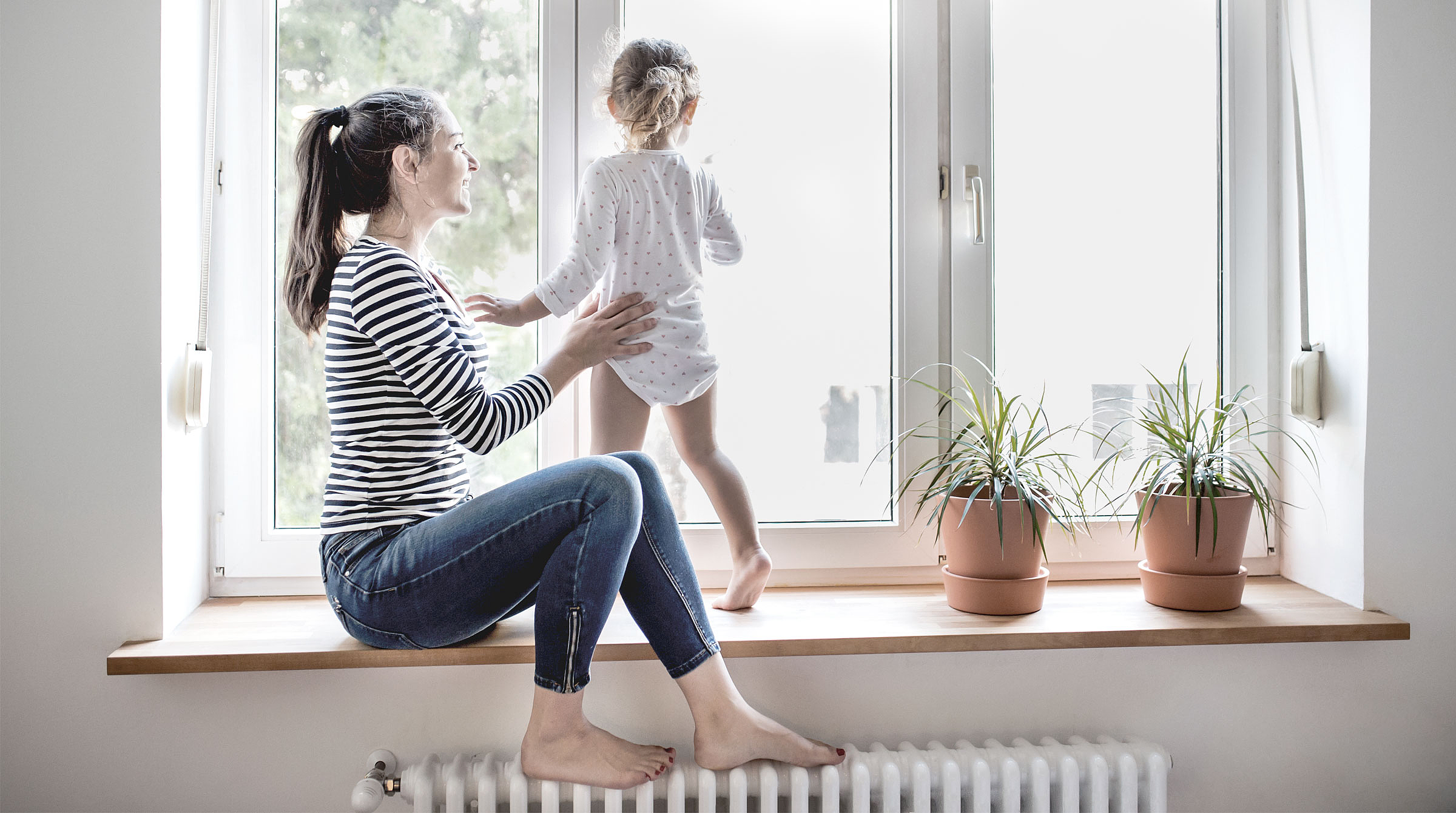 Mutter mit Kind vor einer großen Glasfläche: Eine Glasversicherung schützt vor Kosten bei Glasbruch