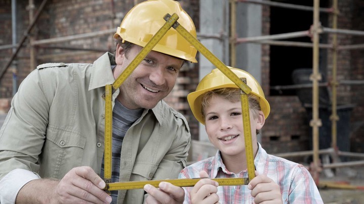 Vater und Sohn sind auf einer Baustelle und halten einen Messstab