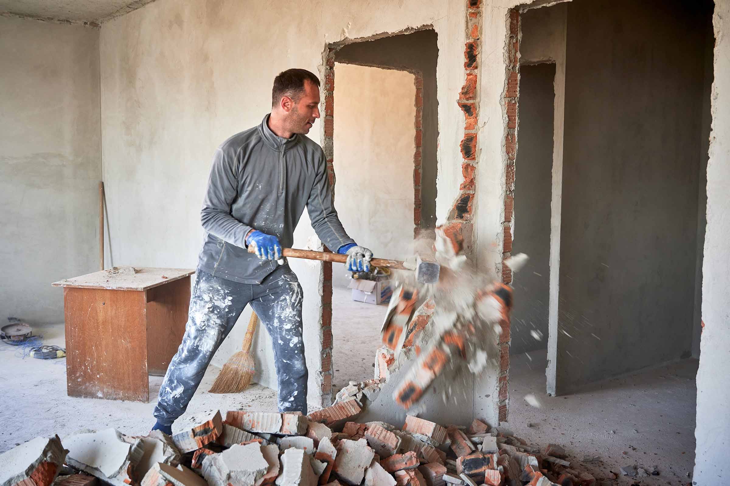 Ein Mann zerstört eine Wand mit einem Vorschlaghammer im Rahmen einer Kernsanierung 