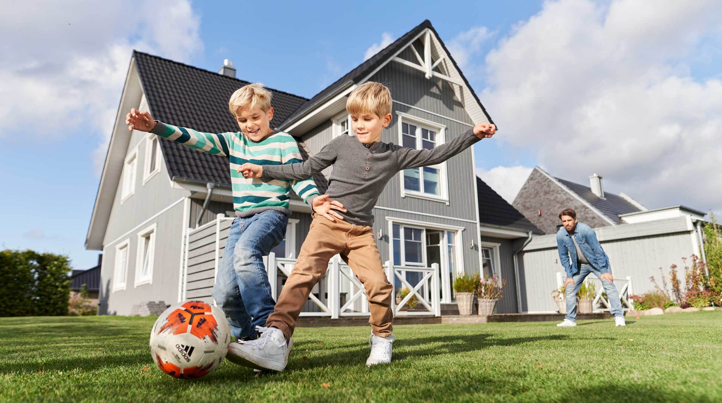 Hausbau planen, zwei Jungs spielen Fußball vor Einfamilienhaus