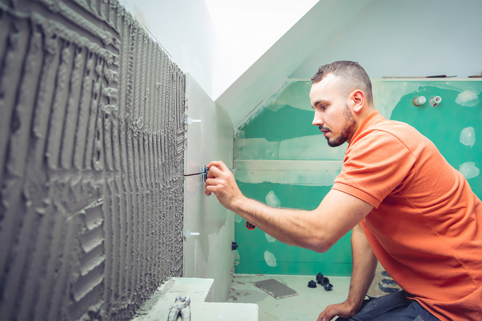 Handwerker klebt Badefließen an die Wand während einer Badsanierung