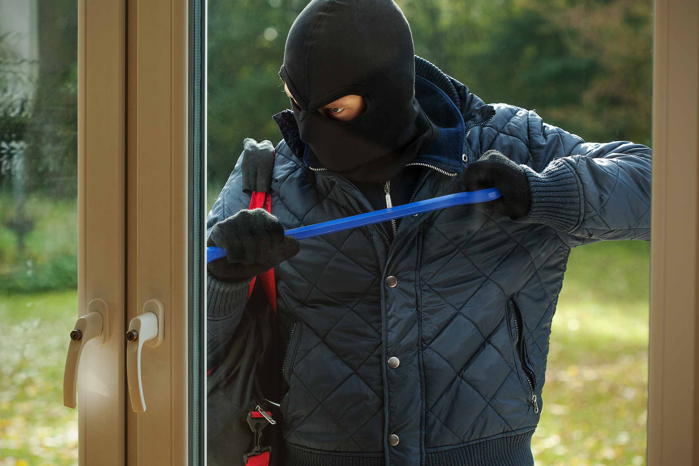 Ein dunkel gekleideter Mann versucht mit einer Brechstange eine Tür zu einem Haus aufzubrechen, um dort einzubrechen.